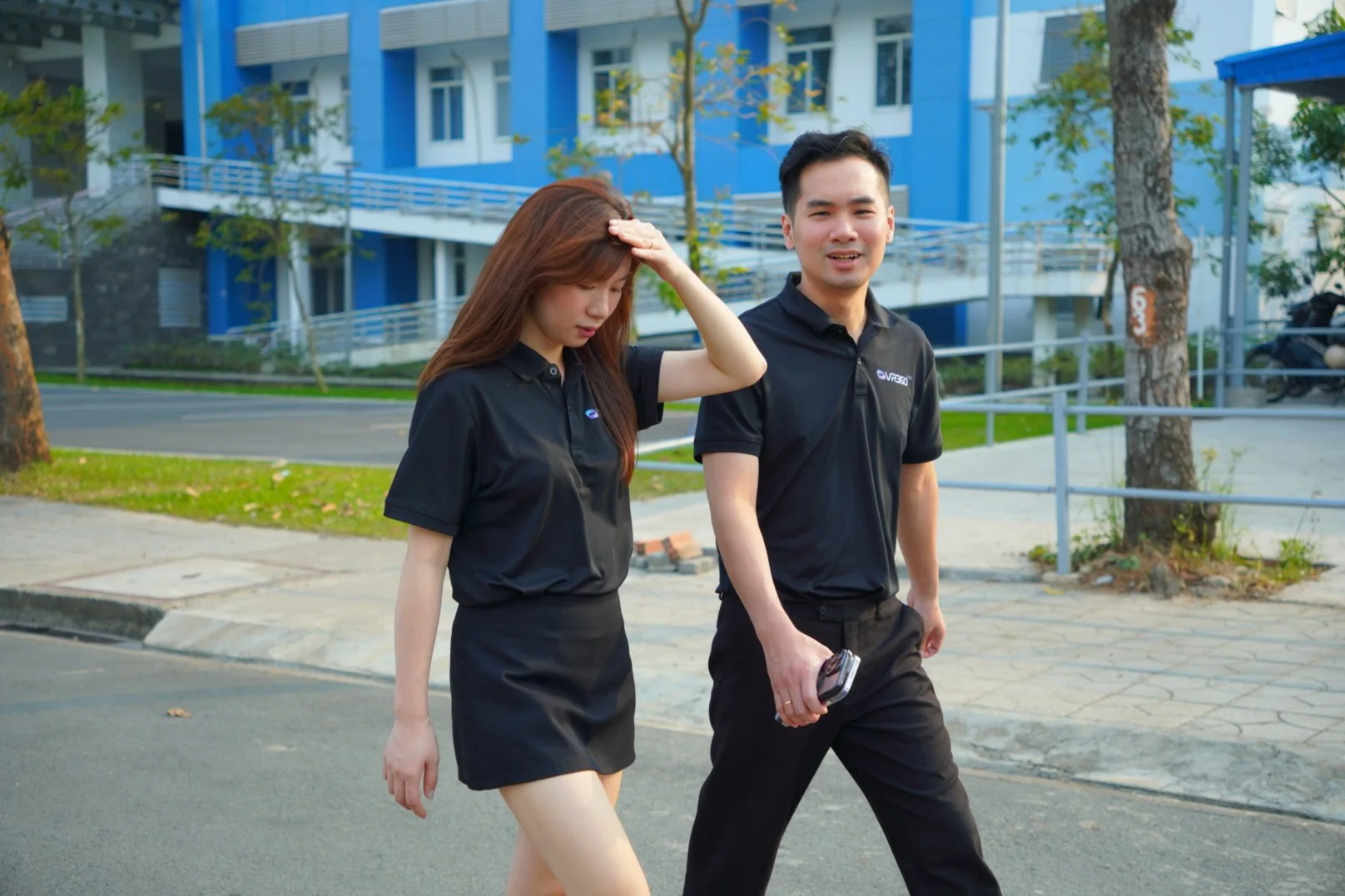 Hai nhân viên đi bộ trên đường nội bộ giữa các tòa nhà trong khuôn viên trường đại học